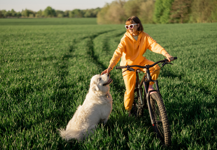 woman on bike in grass field petting dog